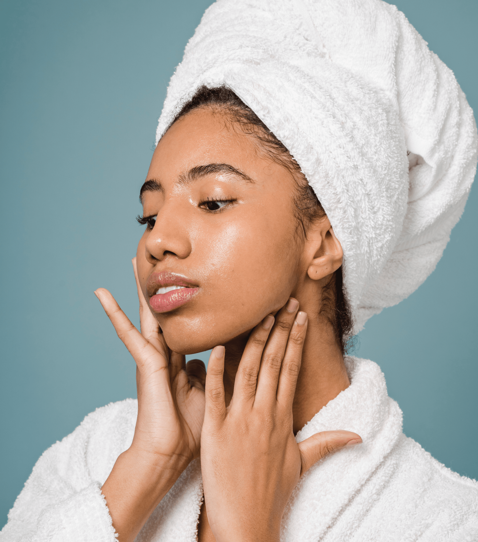 Dark skinned woman wearing a towel on her wet hair and a robe while gently touching her skin
